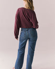 Back full body view of model wearing the Hartt long sleeve tee in fig (deep purple) with clean silhouette and blue jeans, against a plain background.