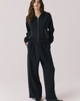 Full body view of woman wearing Chaser’s Kiki True Black Zip Up Hoodie with sequined shoulder accents and matching Daze True Black Joggers on a white background