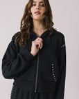 Front view of woman wearing Chaser’s Kiki True Black Zip Up Hoodie with sequin accents on the shoulders and pockets on a white background