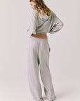 Full body back view of woman wearing Chaser’s Daze Heather Grey Joggers and matching Kiki Heather Grey Zip Up Hoodie on a white background