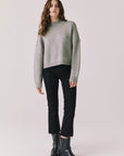 Full body view of woman wearing Chaser’s Frankie Heather Grey Pullover Sweater with black pants and black boots on a white background