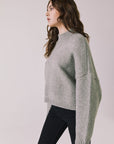 Side view of woman wearing Chaser’s Frankie Heather Grey Pullover Sweater with black pants on a white background