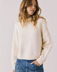 Front view of woman wearing Chaser’s Frankie Warm White Pullover Sweater with blue jeans on a white background