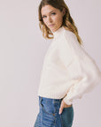 Side view of woman wearing Chaser’s Frankie Warm White Pullover Sweater with blue jeans on a white background