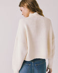 Back view of woman wearing Chaser’s Frankie Warm White Pullover Sweater with blue jeans on a white background