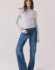 Full body view of woman wearing Chaser’s Owen Moonstone Grey Long Sleeve top and blue jeans on a light gray background