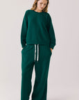 Full body view of woman wearing Chaser’s Cello Blue Grass Green Pullover with matching Hazel Joggers on a white background