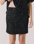 Front view of woman wearing Chaser’s Jayde True Black Mini Skirt with matching Davis True Black Tee on a light gray background