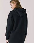 Back view of woman wearing Chaser Aster True Black Hoodie Dress on a plain background