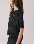 Side view of woman wearing Chaser’s Davis True Black Tee and matching Jayde True Black Mini Skirt on a light gray background