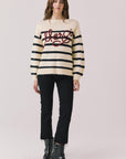 Full body view of woman wearing Chaser’s striped Merci Long Sleeve Sweater with “merci” burgundy red text, black pants, and black boots on a white background