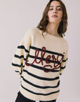Front view of woman wearing Chaser’s striped Merci Long Sleeve Sweater with “merci” burgundy red text on a white background