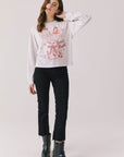 Full body view of woman wearing Chaser’s Spirits Bright Light Grey Long Sleeve with red graphics and text, black pants, and black boots on a light gray background