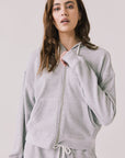 Woman wearing the Abilene Light Heather Grey Zip Up Hoodie with matching pants on a white background