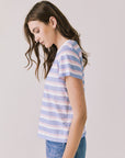 Side view of woman wearing Chaser’s Cosmo Pink Stripes Tee with pink stripe pattern and blue jeans on a white background