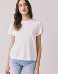 Front view of woman wearing Chaser’s Cosmo White Tee with short sleeves and light blue jeans on a plain background