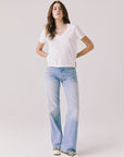 Full body view of woman wearing Chaser’s Gimlet White Tee with blue jeans on a plain background