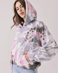 Side view of woman wearing Chaser’s Heart Tie Dye Zip Up Hoodie with heart embroidery detail and hood up on a white background