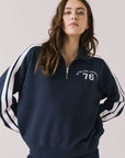Woman wearing Chaser's navy Atelier Sports 76 Half Zip Long Sleeve with white stripes on a light gray background