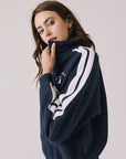 Side view of woman wearing Chaser's navy Atelier Sports 76 Half Zip Long Sleeve with white stripes on a light gray background