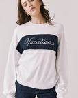 Front view of woman wearing Chaser’s white Vacation Long Sleeve with red ‘Vacation’ text on a light background