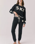 Full body view of woman wearing Chaser’s Heart True Black Joggers with matching “SKI” pullover on a white background