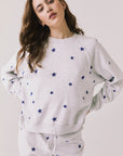 Front view of woman wearing Chaser’s Festive Stars Pullover in Light Grey with star patterns on a white background