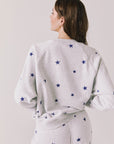 Back view of woman wearing Chaser’s Festive Stars Pullover in Light Grey with star patterns on a white background