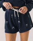 Front view of woman wearing Chaser’s navy Tossed Bows Shorts with small bow prints on a white background
