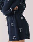 Side view of woman wearing Chaser’s navy Tossed Bows Shorts with allover bow pattern on a white background