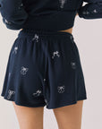 Back view of woman wearing Chaser’s navy Tossed Bows Shorts with allover bow pattern on a white background