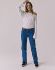 Full body view of a woman wearing Chaser's Ash White Long Sleeve and blue jeans against a plain background