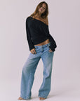 Full body view of a woman wearing Chaser off-shoulder Ash Black Long Sleeve and blue jeans against a plain background