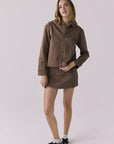Full body view of a woman wearing the Chaser brown All Day Cognac Wash Button Down with matching Sloane Mini Skirt against a plain background