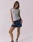 Full body view of a woman wearing Chaser's heather gray button-up Anchor Tee and the Sloane Mini Skirt against a plain background