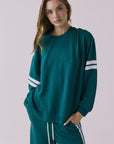 Front view of a woman wearing Chaser's Cornell Pullover in Teal and White with striped sleeves on a plain studio background