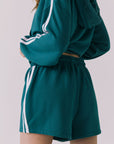 Back view of a woman wearing Chaser's Hanoverr Teal and White Shorts in a clean full body against a plain background