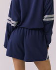 Back view of a woman wearing Chaser's navy blue Cornell Sapphire & Heather Grey Hanoverr shorts on a plain background