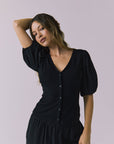 Chaser Abbie Black Blouse shown with matching Lee Trousers in a soft half body pose with the model lifting her arm