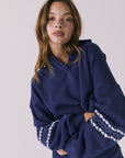 Front view of woman wearing Chaser's navy blue Heart Stitches Pullover Hoodie with arms crossed on a plain background