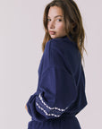 Back view of woman wearing Chaser's navy blue Heart Stitches Pullover Hoodie on a plain background