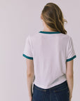 Back view of a woman wearing Chaser's white Coca Cola The Real Thing tee and blue jeans on a plain background