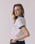 Back view of a woman wearing Chaser's white Coca Cola The Real Thing tee and blue jeans on a plain background