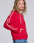 Model wearing Chaser's Cherry Bomb Emily Zip-Up in Cherry Bomb red hooded zip-up with contrast sleeve stripes, angled view