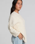 Side view of a woman wearing the Chaser Antique White Harpur Pullover on a neutral background with blue jeans