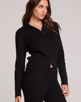 Side angle view of a woman wearing the Chaser Beatrix Black Sweater on a neutral background with black pants