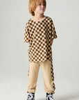 A full body front view of a boy wearing the Chaser Boys Solara Check Tee on a neutral background
