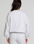 Back view of a woman wearing the Chaser Cashbah Heather Grey Pullover and grey pants on a neutral background