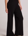 Side view of a woman wearing the Chaser Eliza Black Pants and shoes on a neutral background