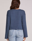 Back view of a woman wearing the Chaser Lunnah Dark Denim Top and blue jeans on a neutral background